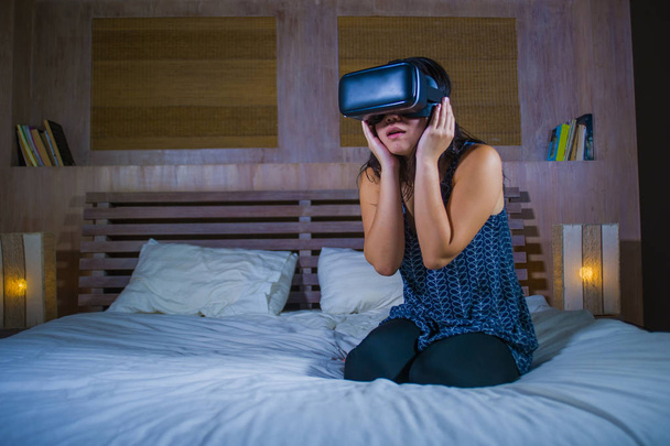 jovem atraente animado e feliz menina vestindo VR realidade virtual jogo fone de ouvido desfrutando espantado a experiência digital 3D assistindo e tocando a ilusão na cama
 - Foto, Imagem
