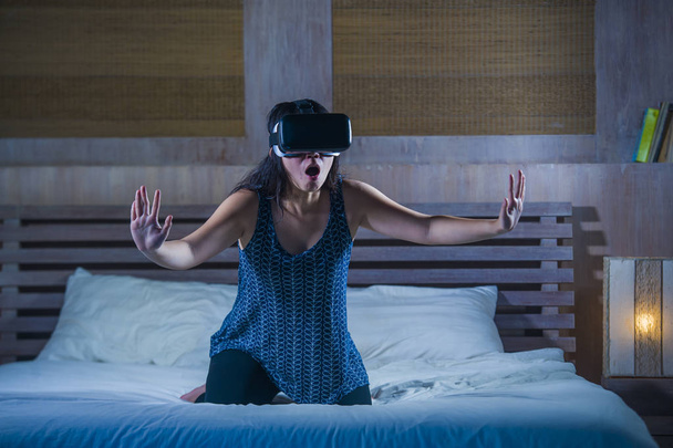 young attractive excited and happy girl wearing VR virtual reality gaming headset playing enjoying amazed the digital 3D experience watching and touching the illusion on bed - Foto, afbeelding