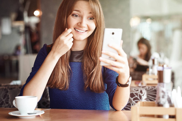 Young business woman using her smart phone and smiling in coffee shop. - Фото, зображення