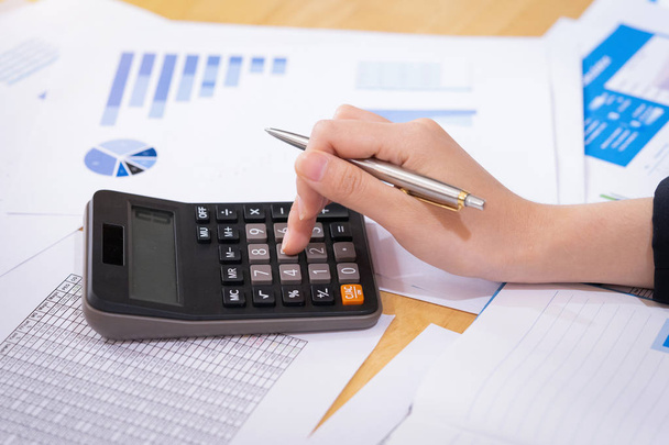 Businesswoman holding a pen and analyze the marketing plan with calculator on wood desk in office. Finance concept. - Photo, Image
