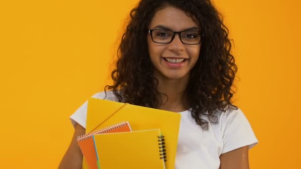Smart college student in eyeglasses holding books yellow background, education - Кадры, видео