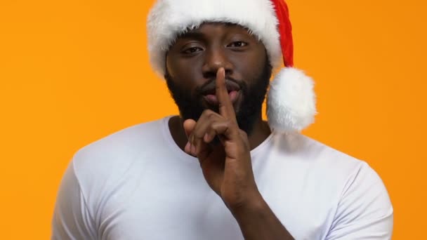 Bearded black male in holiday hat doing silence gesture and showing present box - Filmagem, Vídeo