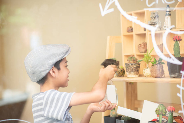Маленький хлопчик поливає кактус в магазині
 - Фото, зображення