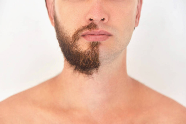 halb rasiert. ein junger Mann mit Bart auf der Hälfte des Gesichts auf hellgrauem Hintergrund.  - Foto, Bild
