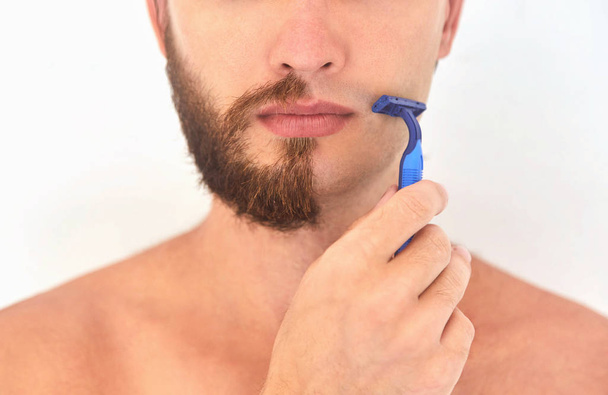 Medio afeitado. Un joven con barba en la mitad de la cara sobre fondo gris claro
.  - Foto, Imagen