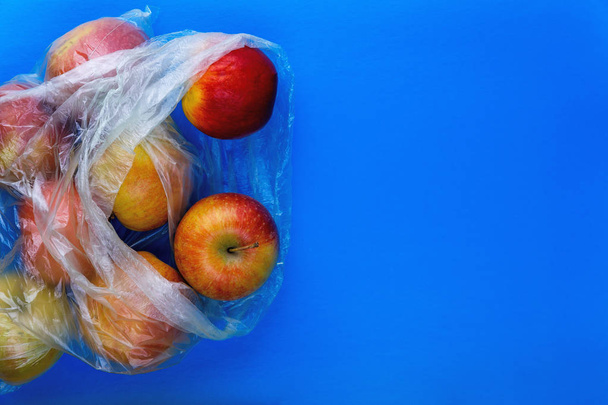environmental concept. Polyethylene packaging is dangerous for the environment. Cellophane grocery bag  with red apples  - 写真・画像