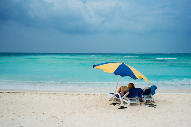 Descanse en una isla tropical. Acuéstese en una tumbona en la playa bajo un paraguas
 - Foto, imagen