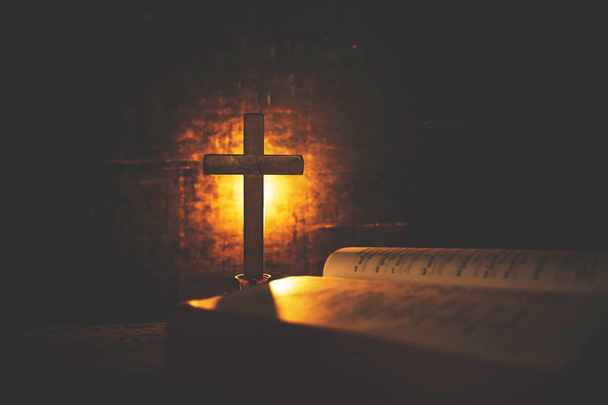 Cross with bible and candle on a old oak wooden table. Beautiful gold background. Religion concept. - Photo, Image