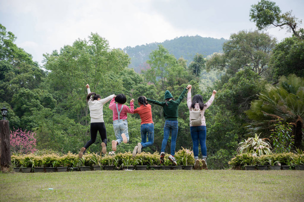 Grupa przyjaciół razem skacząc na greensward i zabawie. Młodych kobiet korzystających na wakacje na świeżym powietrzu. - Zdjęcie, obraz