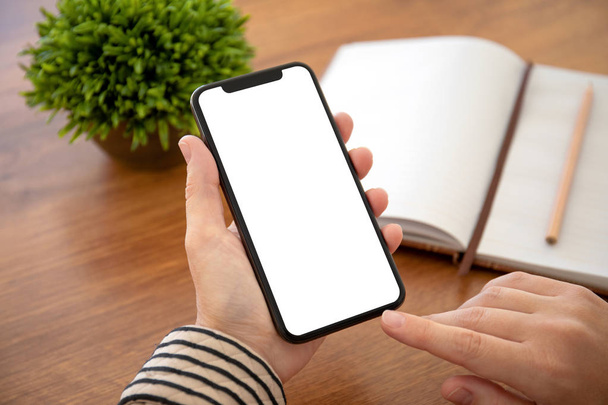 female hands holding phone with isolated screen above the table in office - Foto, Bild