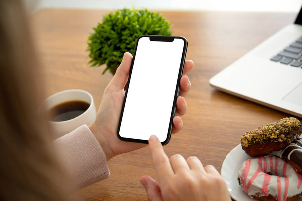 female hands holding phone with isolated screen above the table in the office - Фото, изображение