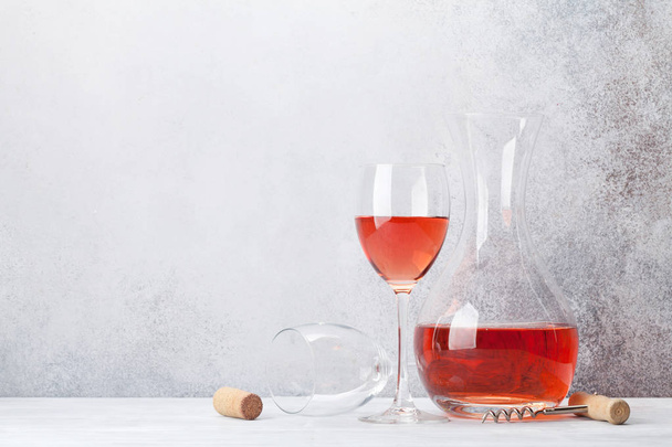 Τριαντάφυλλο κρασί σε ποτήρι και καράφα σε ξύλινο τραπέζι. Μπροστά από το πέτρινο τοίχο με χώρο για το κείμενό σας - Φωτογραφία, εικόνα