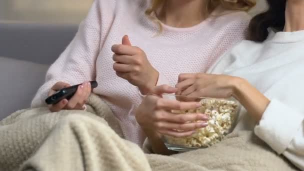 Two pretty friends sitting on sofa eating popcorn and laughing at comedy film - Záběry, video