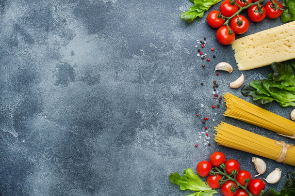 Raw Italian pasta spaghetti and cooking ingredients cherry tomatoes Cheese greens. Italian food dark stone background. Top view with copy space. - Foto, immagini