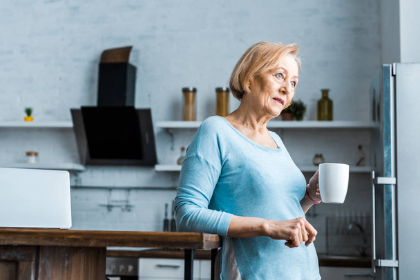 senior woman with cup of coffee looking away in kitchen with copy space - Foto, immagini
