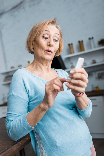 selective focus of surprised senior woman using smartphone at home - Zdjęcie, obraz