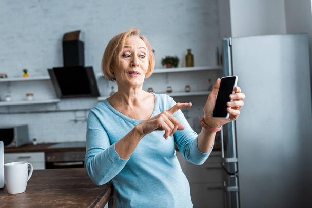 surprised senior woman pointing with finger at smartphone at home - Foto, Imagem