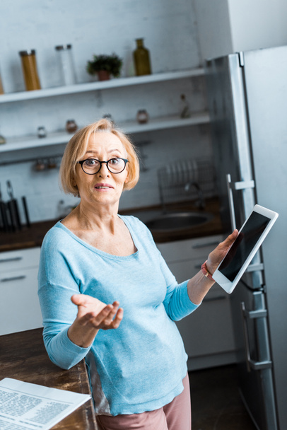 пожилая женщина в очках с помощью цифрового планшета и жеста с рукой на кухне
 - Фото, изображение