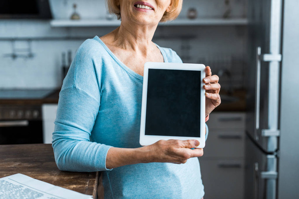 rajattu näkymä vanhempi nainen esittää digitaalinen tabletti tyhjä näyttö kotona
 - Valokuva, kuva