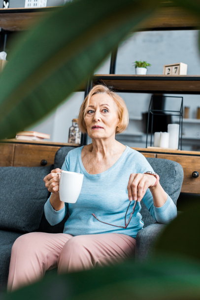 selective focus of senior woman sitting on couch with cup of coffee in living room - 写真・画像