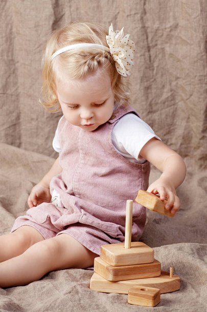 Child girl playing with a wooden toy pyramid. Little cute girl with  natural toys. Copy space - 写真・画像