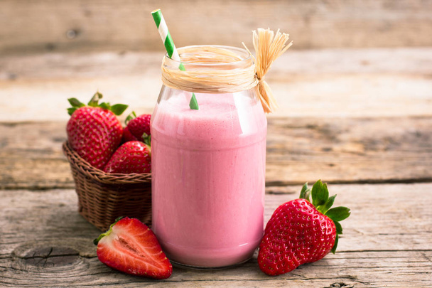 close up view of tasty milkshake drink with strawberries on wooden background - Foto, afbeelding
