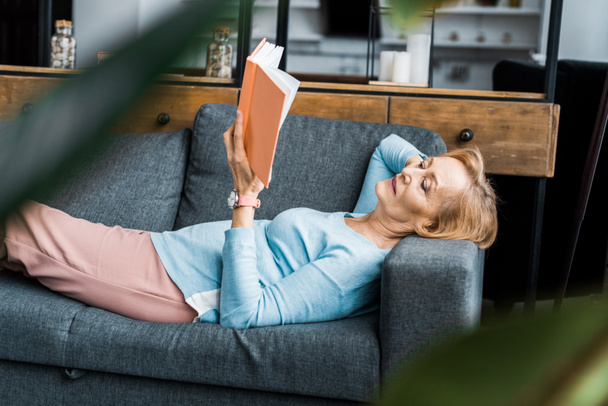 selective focus of senior woman lying on couch and reading book at home  - Photo, Image