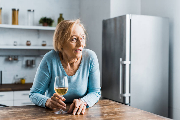 eenzame senior vrouw met glas wijn in de keuken en op zoek weg - Foto, afbeelding