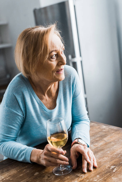 selective focus of senior woman looking away and holding wine glass at home - Fotoğraf, Görsel