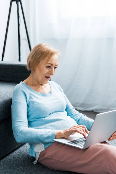 mujer mayor sentada y escribiendo en el ordenador portátil en casa
 - Foto, Imagen