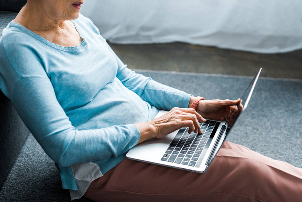 Ausgeschnittene Ansicht einer Seniorin, die zu Hause am Laptop tippt - Foto, Bild