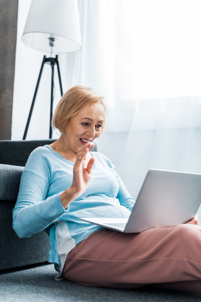 donna anziana sorridente che saluta con mano mentre ha videochiamata sul computer portatile a casa
 - Foto, immagini