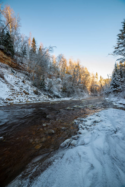 frozen forest river in winter with sandstone cliffs, snow and ice in sunny day - Photo, Image