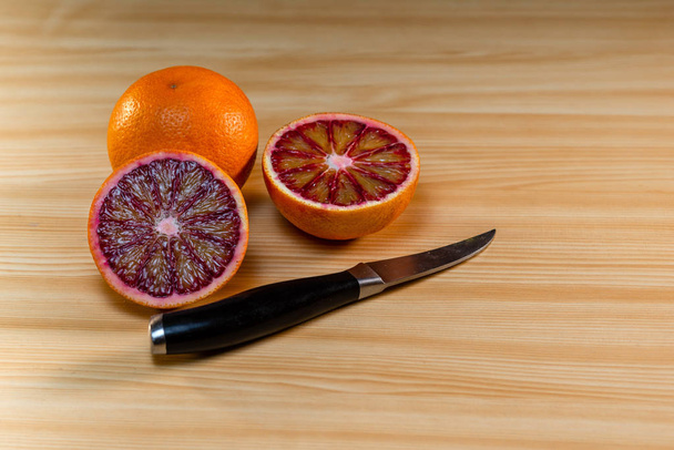 Glass of juice, knife and cut red oranges on a light wooden table.  - Fotoğraf, Görsel