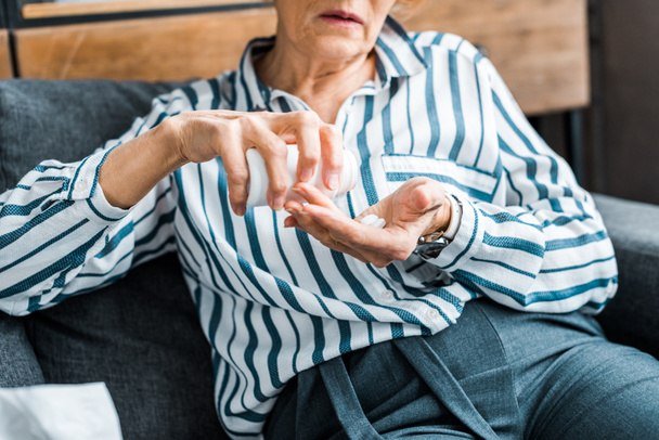 обрезанный вид больной пожилой женщины, сидящей на диване и принимающей таблетки дома
 - Фото, изображение