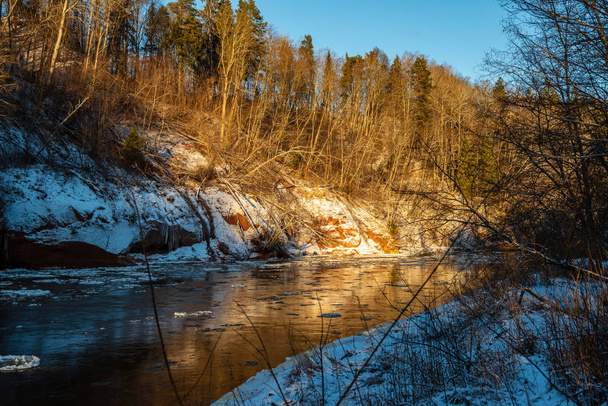 замерзла лісова річка взимку з пісковиковими скелями, снігом і льодом в сонячний день
 - Фото, зображення