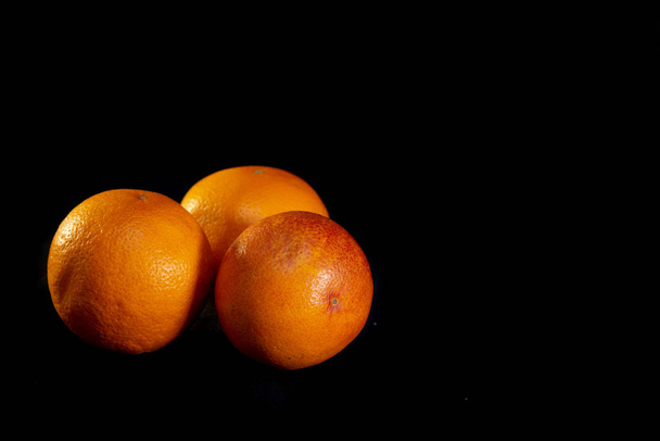 Three red oranges on a black background - image - Foto, imagen