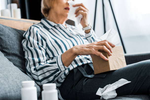 vista parziale di malata donna anziana con naso che cola in possesso di scatola di tessuto a casa
 - Foto, immagini