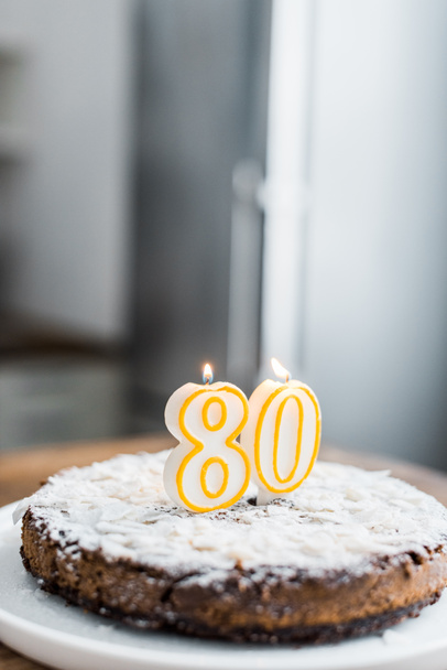 selectieve aandacht van heerlijke verjaardagstaart met brandende kaarsen, kopie ruimte en '80' ondertekenen op bovenkant - Foto, afbeelding