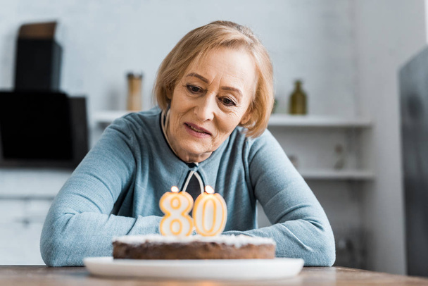 masada oturan ve pastalara '80' işareti ile evde doğum günü kutlaması sırasında arayan yalnız kadın kıdemli - Fotoğraf, Görsel