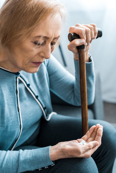 sick senior woman with walking stick holding medicine in hand  - Photo, image