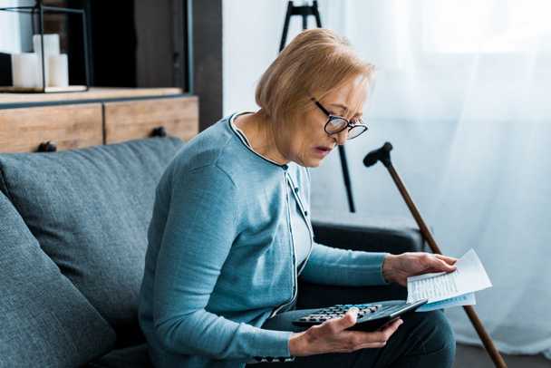 donna anziana seduta sul divano con calcolatrice e conteggio bollette a casa
 - Foto, immagini