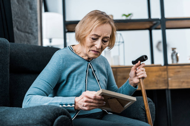 smutné, starší žena sedí s vycházkovou hůl a při pohledu na rámeček obrázku - Fotografie, Obrázek