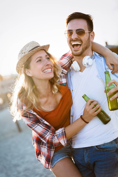 Ευτυχισμένο νεαρό ζευγάρι χαμογελώντας και πίνοντας μπύρα στην παραλία - Φωτογραφία, εικόνα
