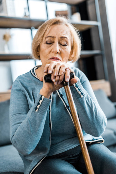 sad senior woman with eyes closed leaning on walking stick at home - Fotoğraf, Görsel