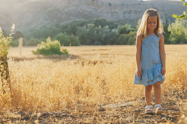 kleine blonde meisje in jurk in veld met heuvels op de achtergrond - Foto, afbeelding