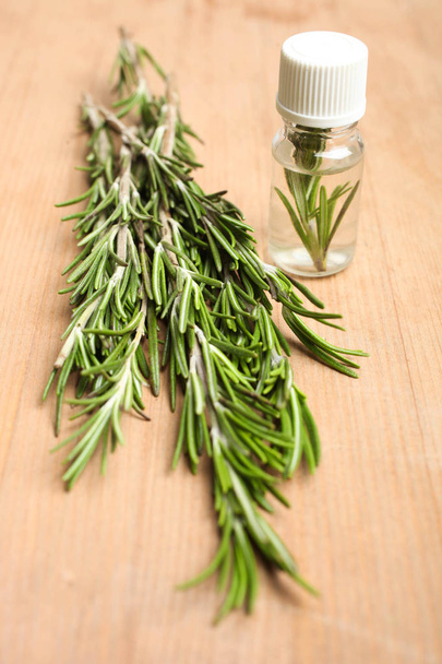 На деревянном фоне зеленая веточка эмаля и бутылка ароматного масла. Концепция ароматерапии, медицины
. - Фото, изображение