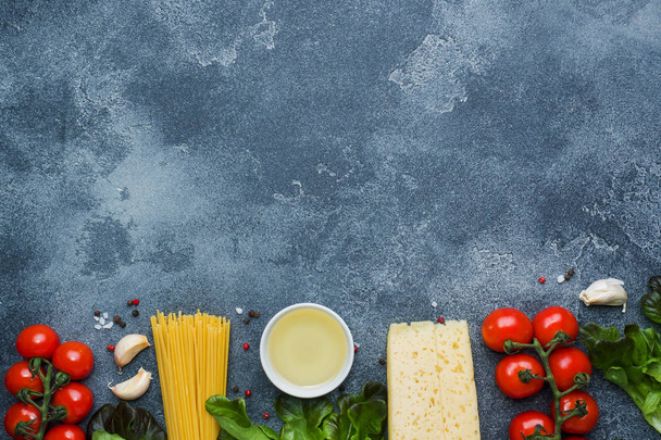 Raw Italian pasta spaghetti and cooking ingredients cherry tomatoes Cheese greens. Italian food dark stone background. Top view with copy space. - Valokuva, kuva