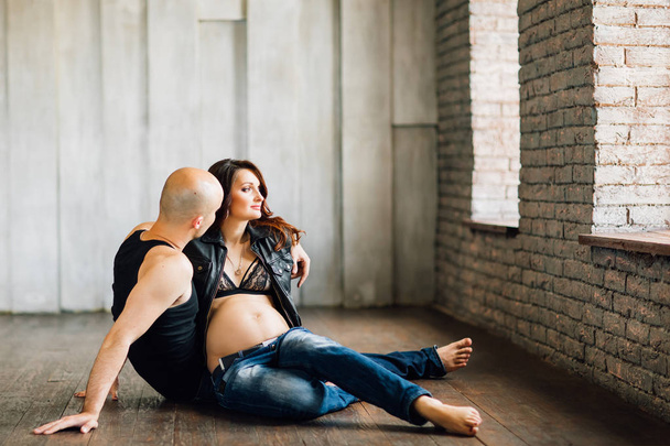 Nuori raskaana oleva nainen, jonka mies istuu lattialla studion ikkunan lähellä
 - Valokuva, kuva