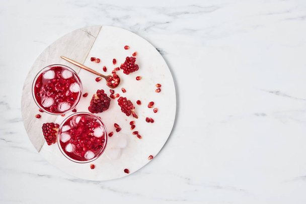 Fresh pomegranate juice with ice and red pomegranate seeds on white marble serving plate over marble background. Top view with copy space for text. Overhead shot. - Foto, Bild
